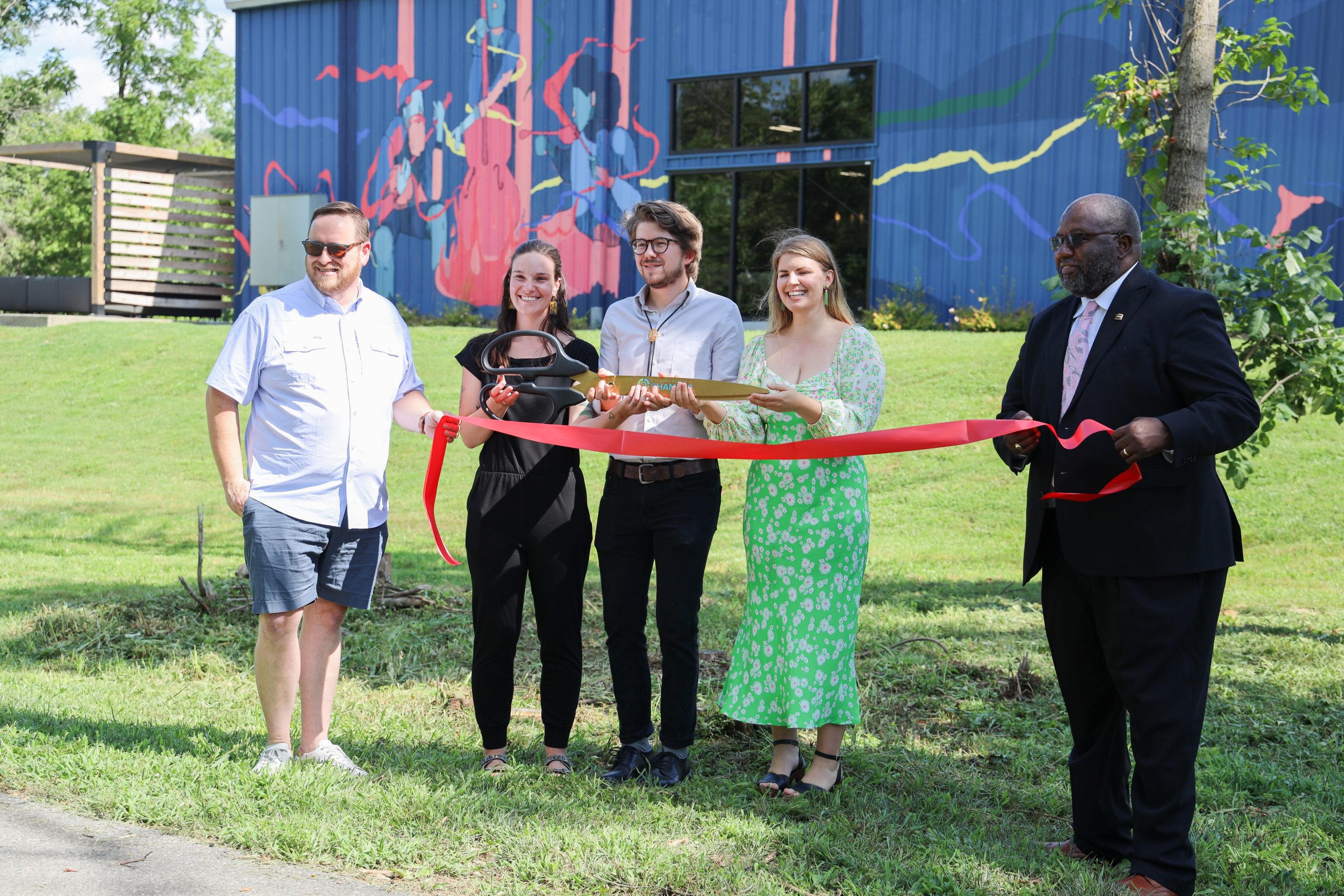 two people holding a red ribbon and three people posing with large scissors